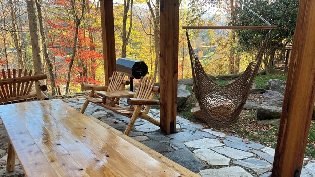 Ein Holztisch mit Bänken, eine Hängematte und ein Grill in einer gepflasterten Außenanlage mit Herbstlaub.