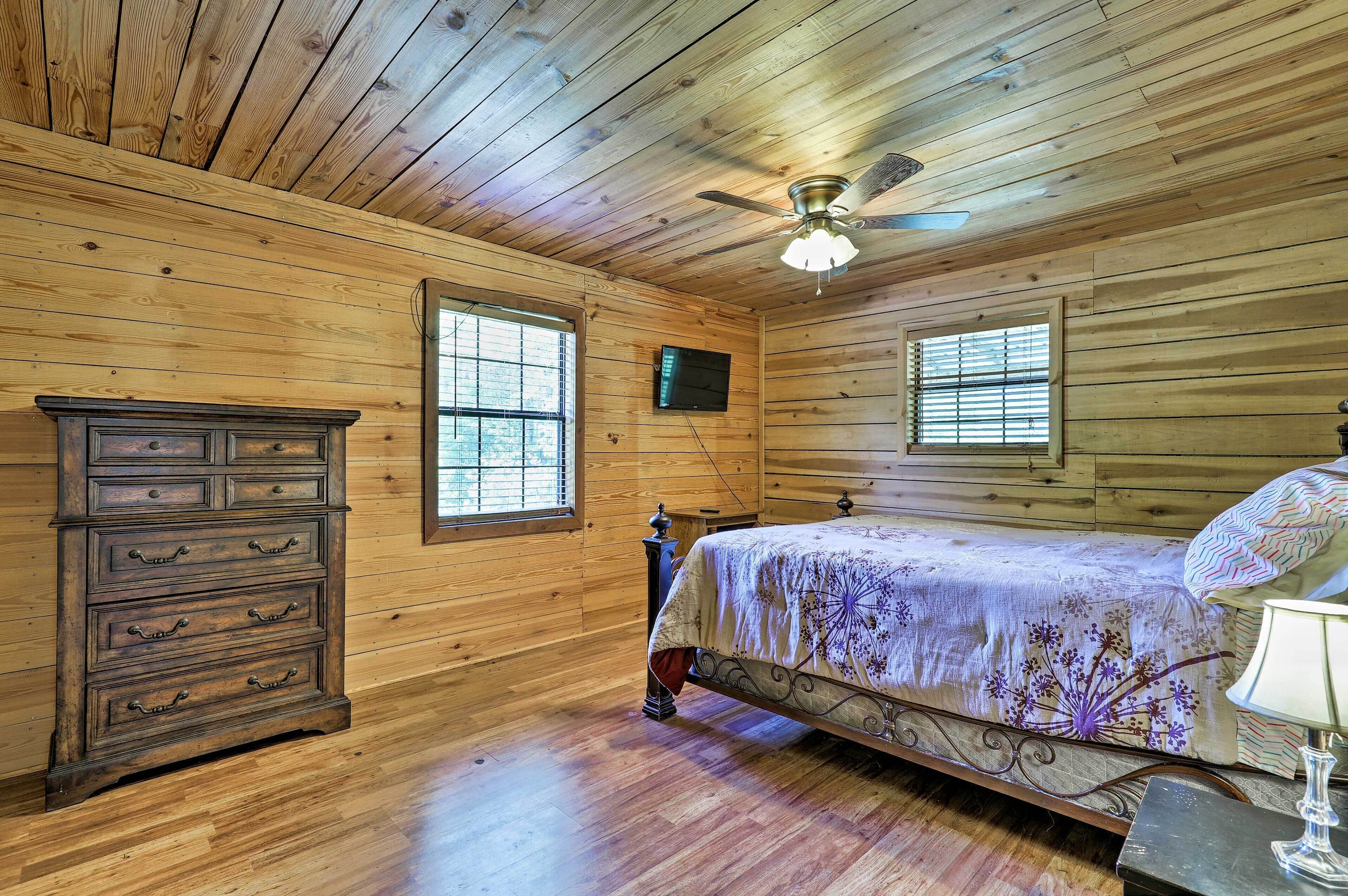 A wooden-paneled bedroom with a bed, dresser, and ceiling fan.