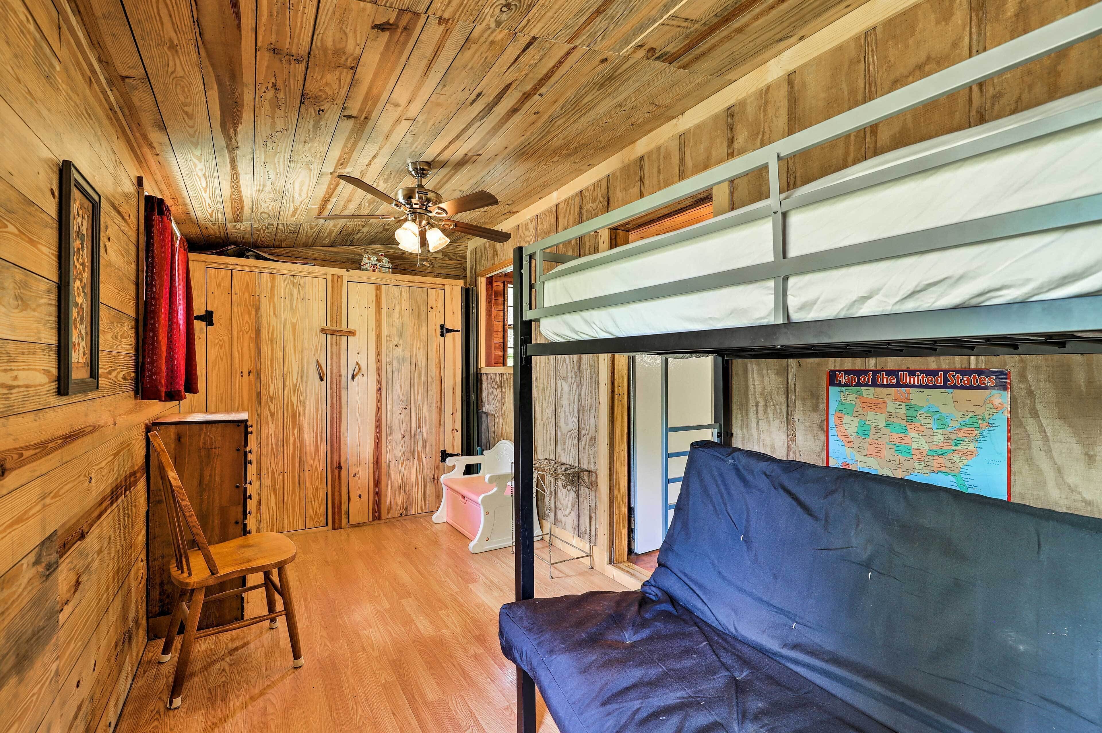 Interior rústico de una cabaña con literas, paredes de madera, un ventilador de techo, una silla de madera y un mapa de Estados Unidos en la pared.