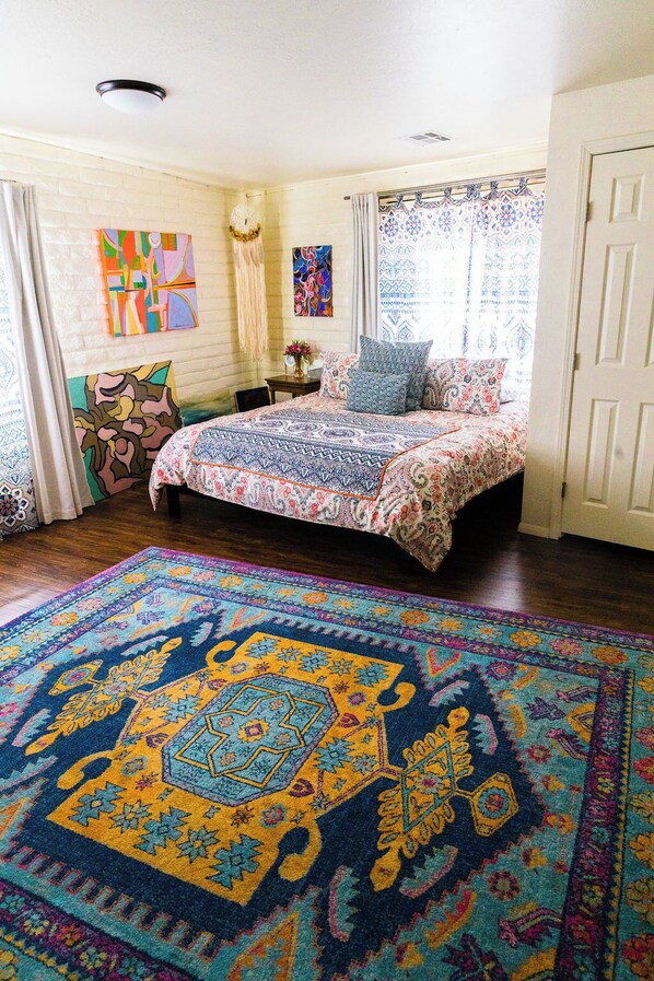 A bedroom with a large bed, a colorful rug, and artwork on the walls.
