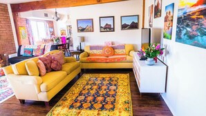 A living room with a yellow sofa, a patterned rug, and a white sideboard with a vase of flowers. - Local Artists Bohemian Loft (Sedona)