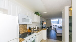 Una cocina moderna con armarios blancos, encimeras de granito y horno empotrado. Hay un comedor con vista a la ciudad.