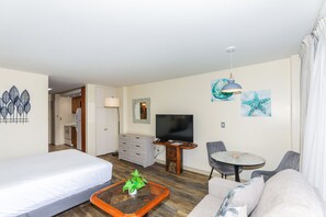 A hotel room with a bed, a sofa, a small dining table, a TV, and a mirror.