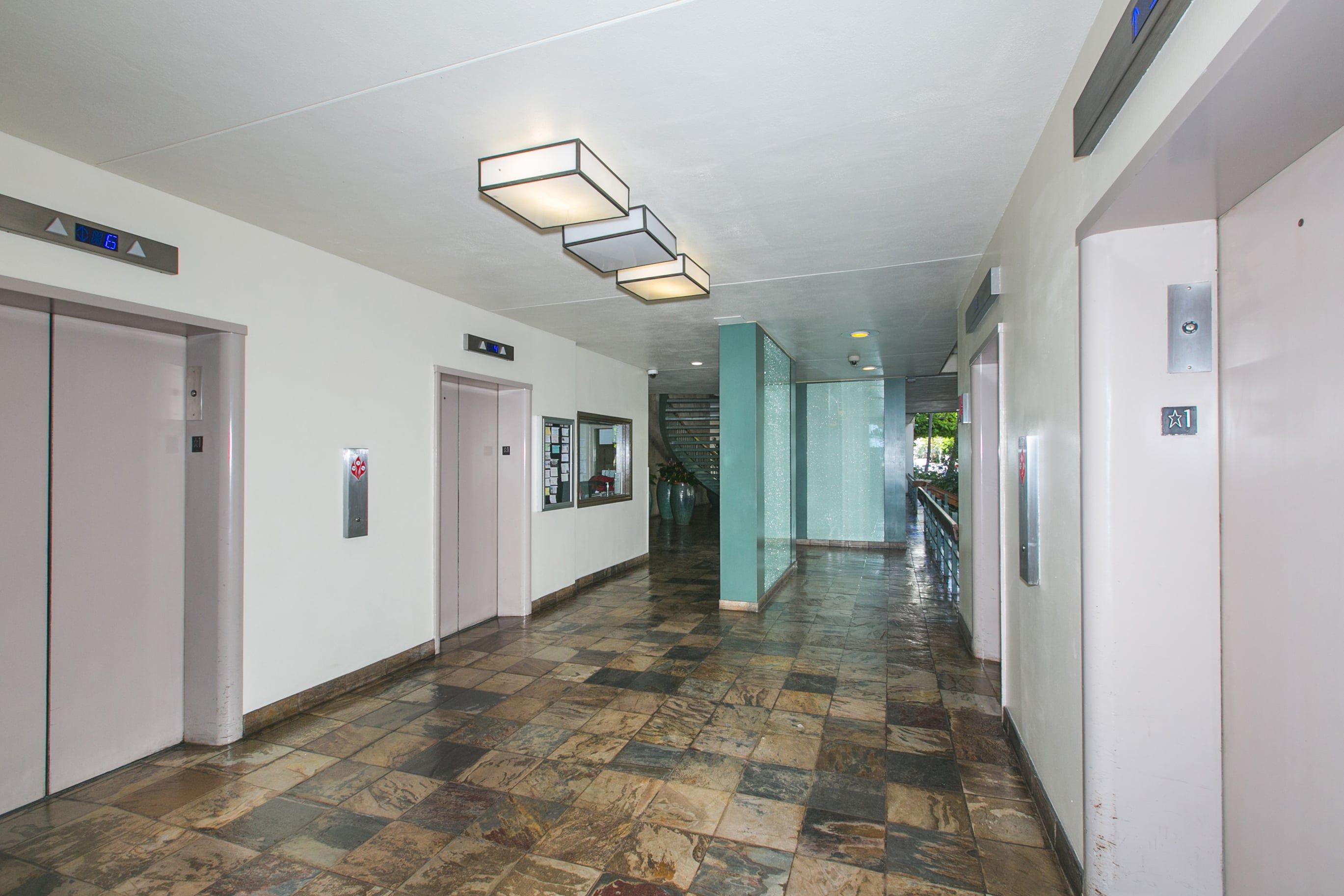 Corredor com elevadores, escada e piso revestido de azulejos.