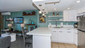 Een moderne keuken met witte kasten, een centraal eiland en een eethoek met tafel en stoelen.