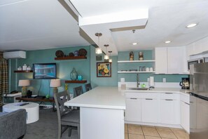 A modern kitchen with white cabinets, a central island, and a dining area with a table and chairs. - Ilikai Hotel - Perfect Waikiki Getaway, Waikiki Oasis!  Minutes to Beach! (Honolulu)