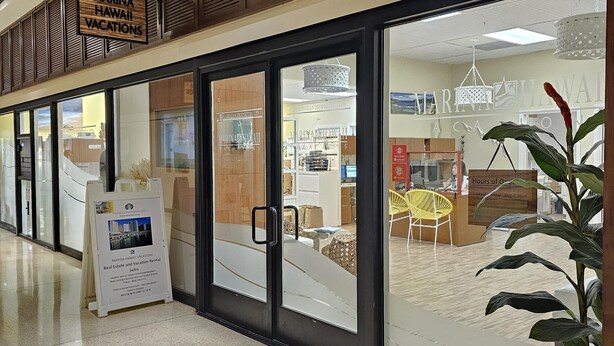 Interior de hotel con mostrador de recepción, un cartel anunciando Marina Hawaii Vacations y un área de recepción con una silla y una planta.