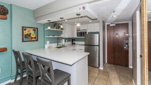 Una cocina moderna con armarios blancos, un refrigerador de acero inoxidable y una zona de comedor con una isla blanca y dos sillas.