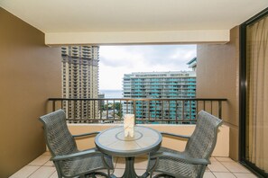 A balcony with a round table and two chairs, overlooking a cityscape with high-rise buildings.