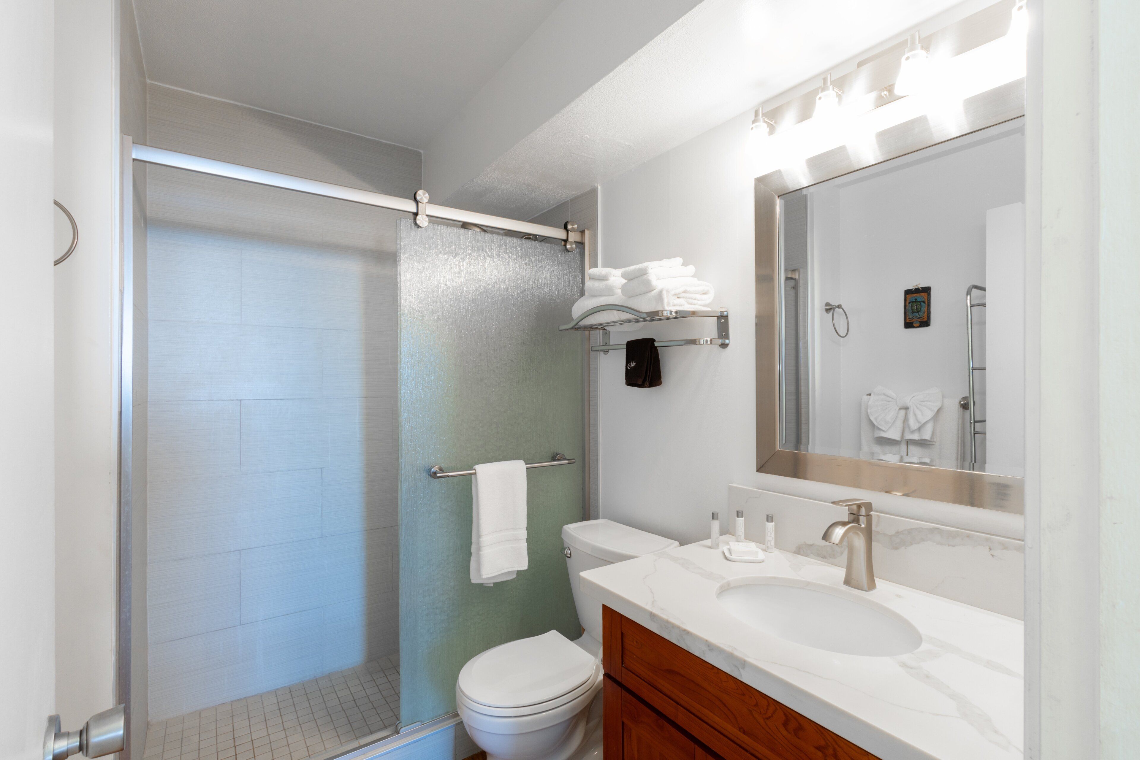 Un baño con ducha, inodoro, tocador y un espejo grande.