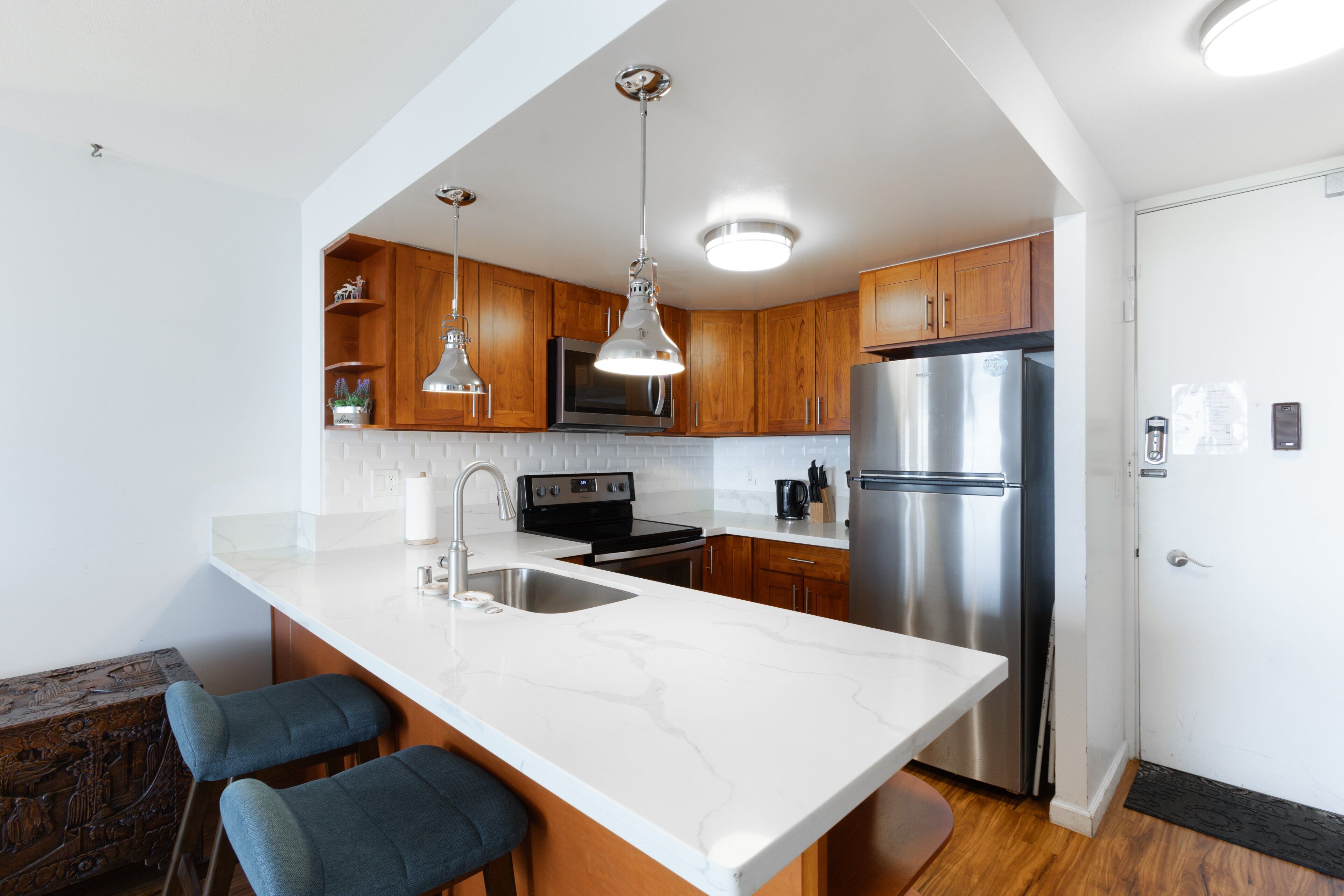 A modern kitchen with a large island, stainless steel appliances, wooden cabinets, and pendant lighting.