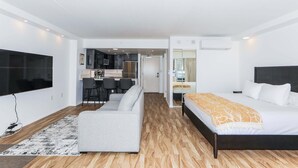 Moderni hotellihuone, jossa on sänky, sohva, televisio ja pieni keittiönurkkaus.