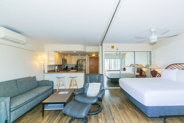 Habitación de hotel con sofá, escritorio, silla, cama, ventilador de techo y una zona de cocina.