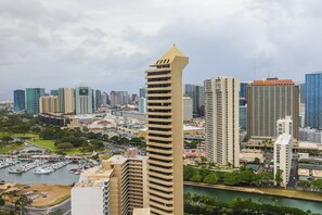 Paisagem urbana com um edifício alto e imponente, destacando um design arquitetônico único, cercado por outros arranha-céus e um calhavete com barcos.