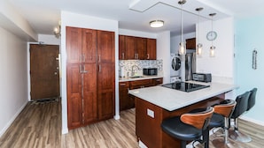 A modern kitchen with wooden cabinets, a central island with bar stools, a microwave, and a refrigerator.