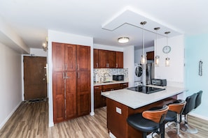 Uma cozinha moderna com armários de madeira, uma ilha central com banquetas, micro-ondas e frigorífico.