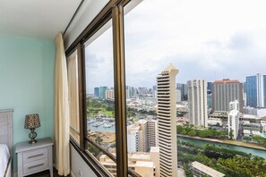 Quarto com uma grande janela que oferece vista para a paisagem urbana, com edifícios altos e um porto de iates.