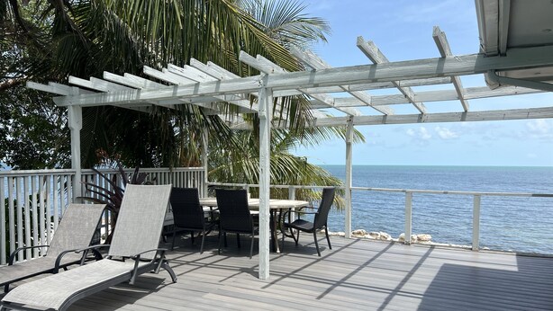 A wooden deck with a pergola, outdoor seating, and a view of the ocean. - Caribbean Sunsets: 3BR Home Gulf Views Pool & Dock (Marathon)