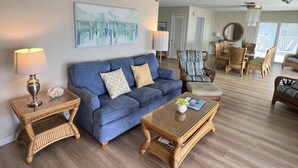 A living room with a blue sofa, a coffee table, and wicker furniture. There is a painting on the wall and a ceiling fan. - Caribbean Sunsets: 3BR Home Gulf Views Pool & Dock (Marathon)