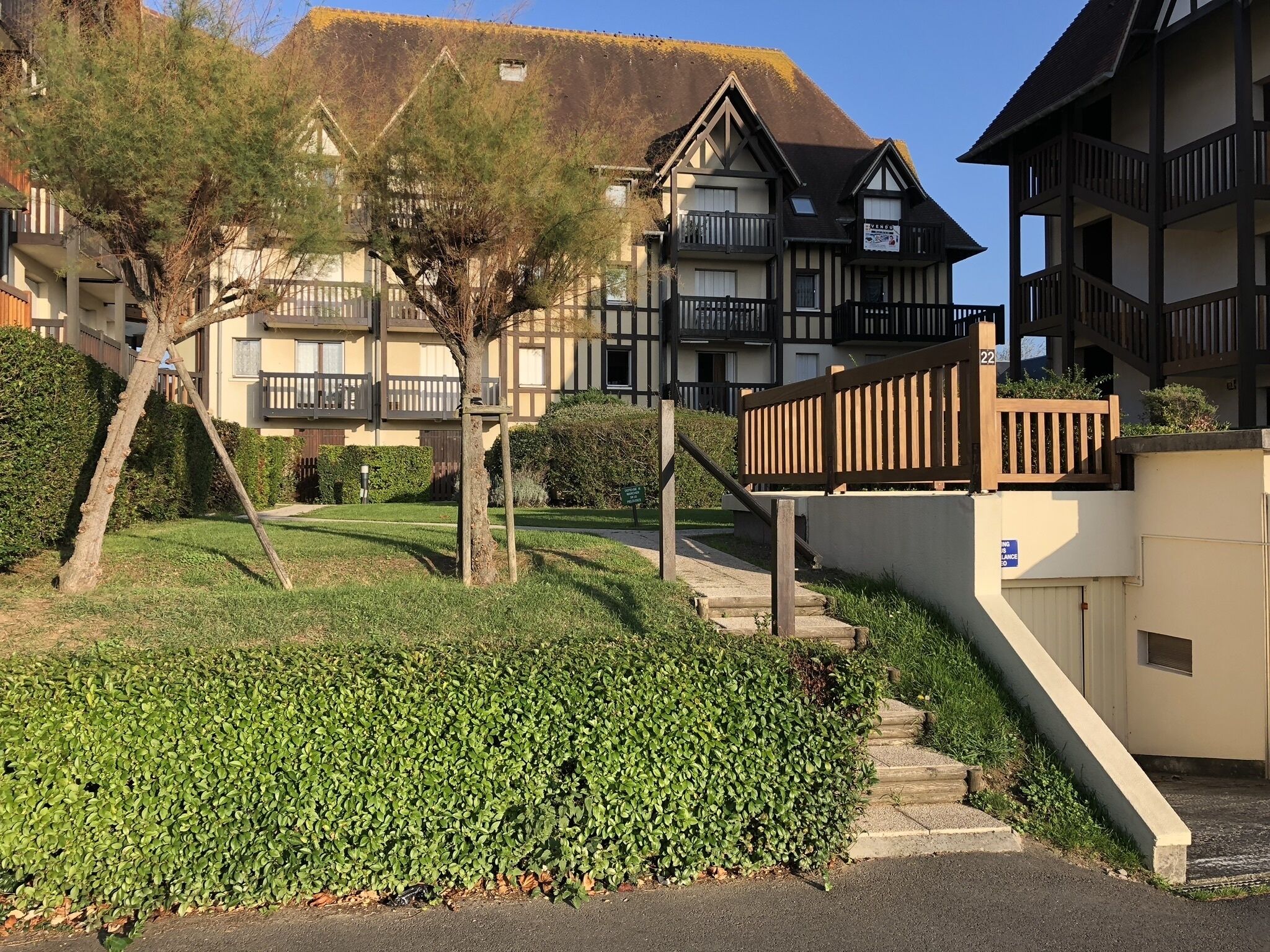 A residential building with a staircase leading to a gated entrance, surrounded by well-maintained hedges and trees.
