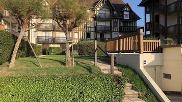 A residential building with a staircase leading to a gated entrance, surrounded by well-maintained hedges and trees.