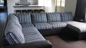 Una sala de estar moderna con un sofá seccional a rayas, una zona de cocina con estufa a gas y un amplio ventanal que proporciona luz natural.