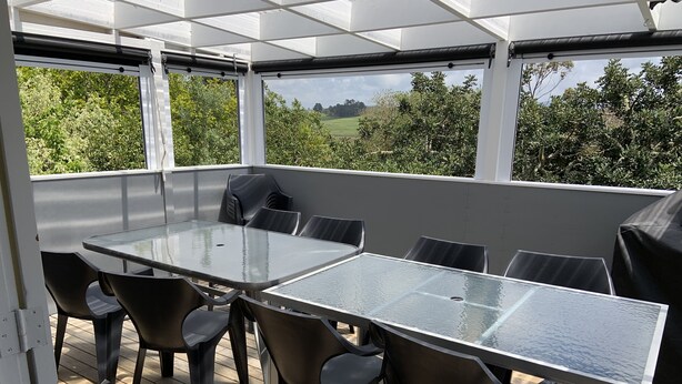 Un patio techado al aire libre con mesa y sillas de vidrio, rodeado por una terraza de madera.
