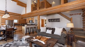 Ein großzügiger Wohnbereich mit hoher Decke, Holzbalken, einer Küche mit Barhocker und einer gemütlichen Sitzecke mit Couchtisch.