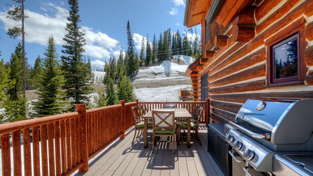Eine Holzterrasse mit Grill und Sitzbereich mit Blick auf eine verschneite Berglandschaft.