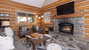 Ein Blockhaushaus-Interieur mit Kamin aus Naturstein, Ledersofas und einem Fernseher, der über dem Kamin angebracht ist.