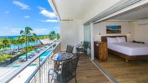 Een balkon met uitzicht op een strand en zwembad, een bed en een kleine tafel met stoelen.