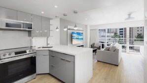 Een moderne keuken met een inbouwoven, een zithoek met een grijze bank en een groot raam met uitzicht op de stad.
