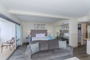 Une chambre d’hôtel moderne avec un grand lit, un canapé gris, une petite table et un miroir.