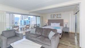 Habitación de hotel con una cama grande, un sofá, un balcón con vistas a la ciudad y un área de comedor.