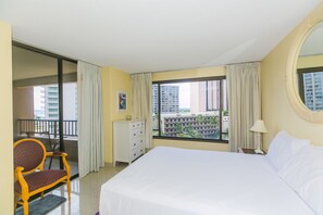 Relax in a spacious room with a large bed, comfortable chair, and stylish dresser, offering a view of the city skyline and palm trees.