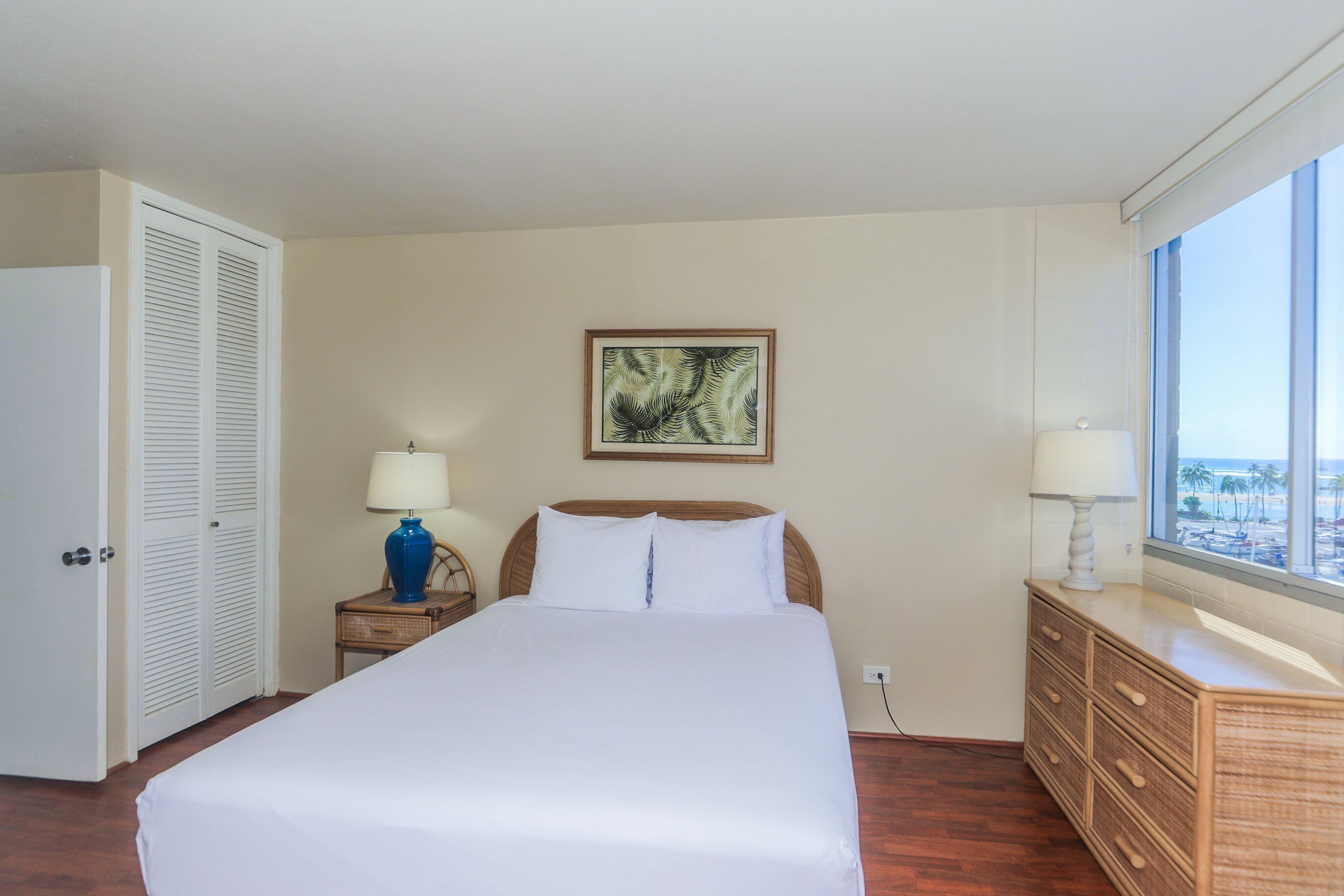 Une chambre d’hôtel avec un grand lit, une table de chevet avec une lampe, une commode et une fenêtre donnant sur un beau paysage.