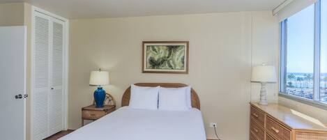 Une chambre d’hôtel avec un grand lit, une table de chevet avec une lampe, une commode et une fenêtre donnant sur un beau paysage.