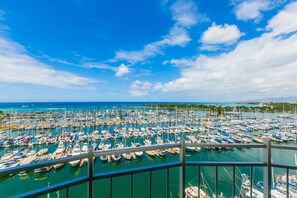 Un port de plaisance rempli de bateaux, un ciel bleu azur et une côte lointaine parsemée de bâtiments et de verdure.
