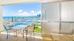 A balcony with a table and chairs, a view of a marina, and a cityscape in the background.