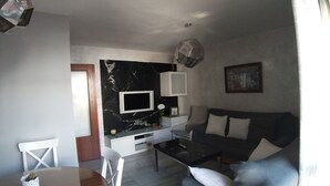 Una sala de estar moderna con un sofá, una mesa de centro, un televisor instalado en una pared de mármol y un comedor con mesa y sillas.