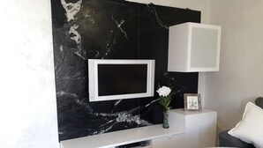 Una sala de estar moderna con pared de mármol, un televisor de pantalla plana montado en una consola blanca, una mesita y un florero con flores.