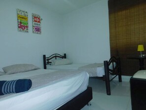 Two single beds with wooden headboards and white bedding, a small table, chair, and wall-mounted shelf.