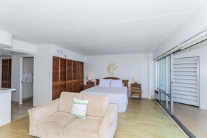 A hotel room with a bed, a sofa, a wooden wardrobe, a decorative wall piece, and a sliding glass door. - Highly desirable Deluxe One-bedroom Yacht Harbor View - Reserve Today, Will not last Long!! (Honolulu)