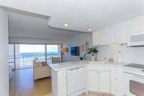 A modern kitchen with white cabinetry, a built-in microwave, and a view of the sea through a balcony.