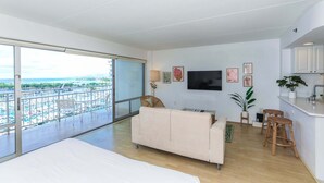 A modern living room with a balcony overlooking a marina, a flat-screen TV, and a kitchen area with bar stools. - Highly desirable Deluxe One-bedroom Yacht Harbor View - Reserve Today, Will not last Long!! (Honolulu)