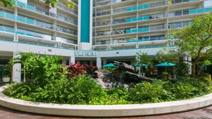 Un hôtel à plusieurs étages doté de balcons, d’un espace paysager avec une fontaine centrale et d’un jardin aménagé.