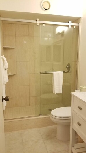 Une salle de bain avec une douche à parois de verre, des toilettes et un meuble-lavabo avec des tiroirs.