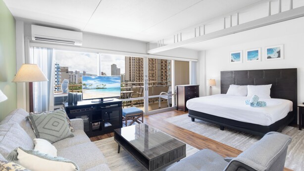 Una habitación de hotel moderna con una cama grande, un sofá, una mesa de centro, un televisor y un balcón con vista a la ciudad.