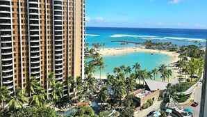 Een hoog hotel met meerdere balkons met uitzicht op een strand met helderblauw water en palmbomen.
