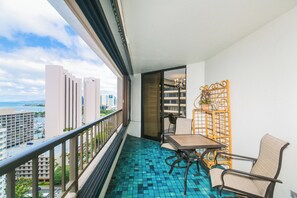 Enjoy the ocean views from this balcony with a cityscape backdrop, featuring a tile floor, wooden table, and comfortable seating.